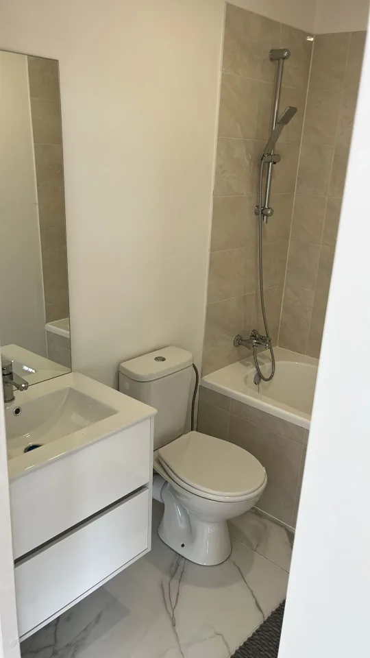 Salle de bain avec meuble vasque et miroir, WC, baignoire avec douche, faïence beige et sol effet marbre