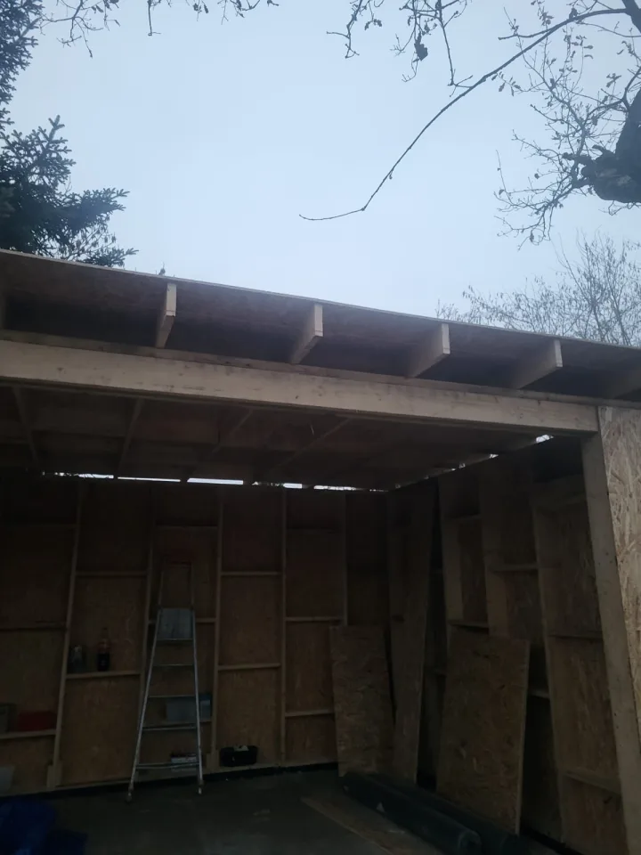 Sous la toiture en cours de pose, poutre, solives et murs en ossature bois fermés de panneaux OSB
