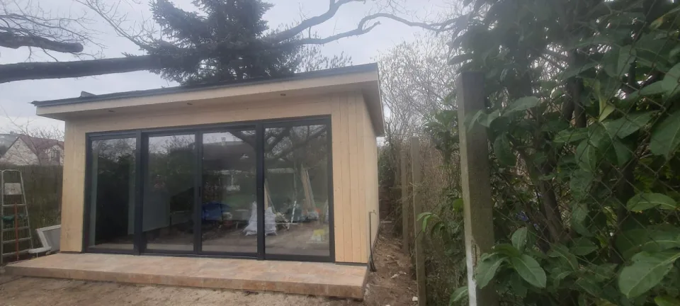 Bardage en bois clair posé et grande baie coulissante vitrée installée, matériaux de fin de chantier encore à l’intérieur