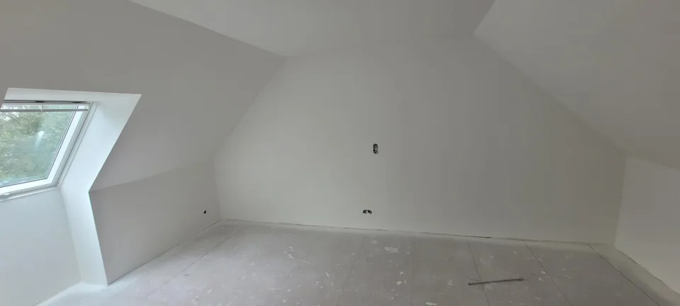 Grande pièce sous les combles, fenêtre de toit à gauche, rampants et mur du fond blancs, boîtiers électriques en attente