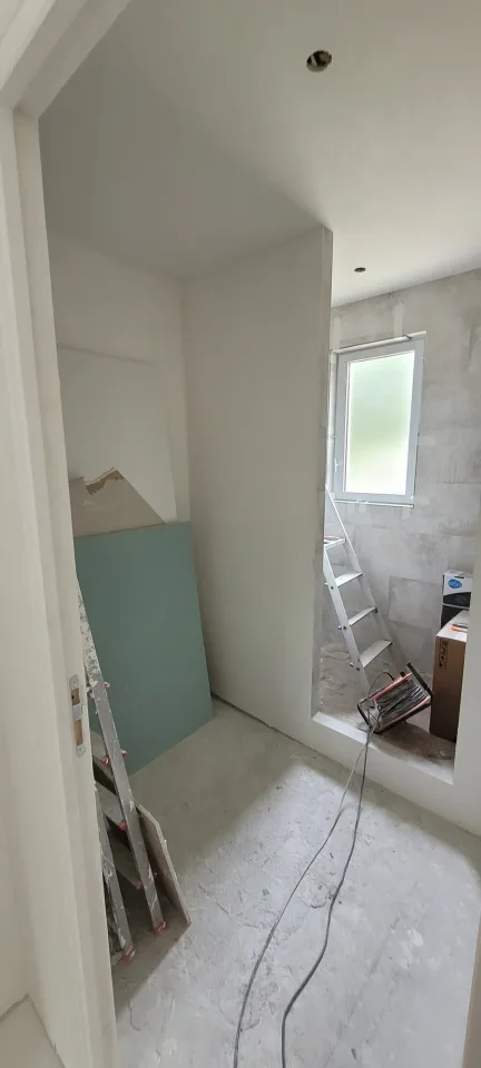 Salle d’eau vue depuis la porte, plaques de plâtre hydrofuges en attente contre le mur et coin carrelé sous la fenêtre au fond