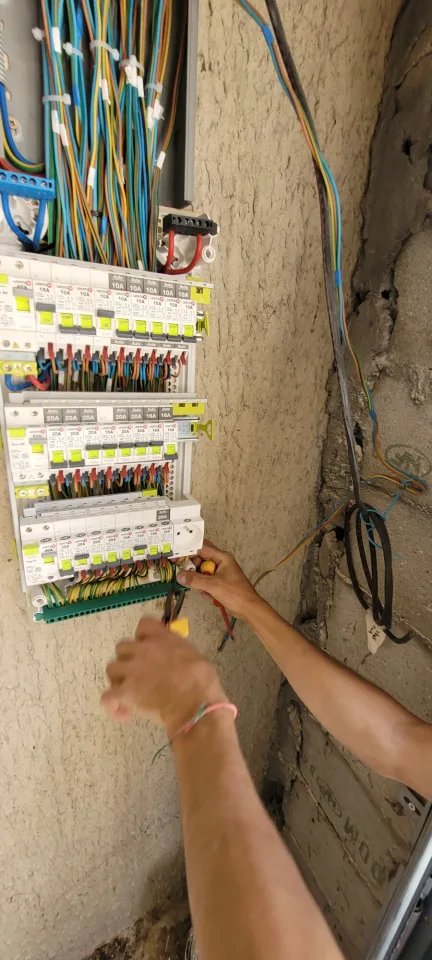 Nouveau tableau électrique en cours de câblage, rangées de disjoncteurs et mains de l’électricien au travail