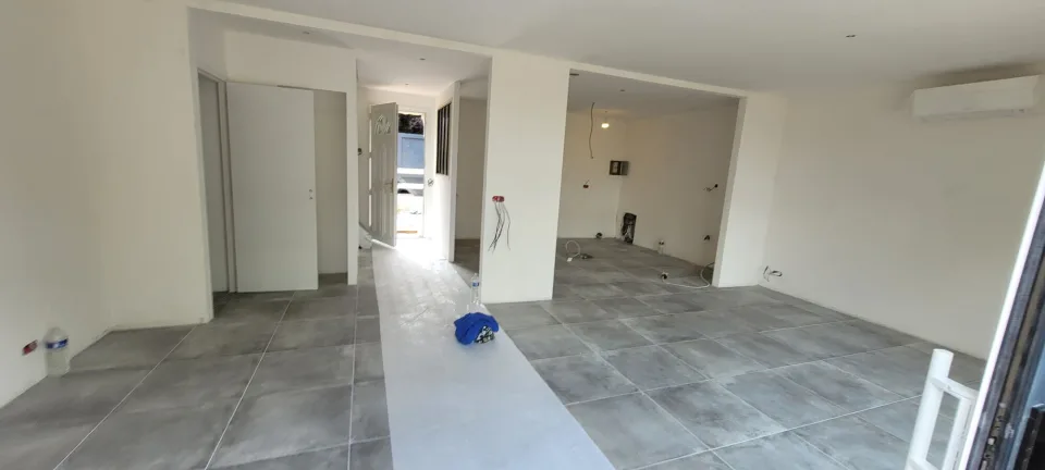 Rez-de-chaussée ouvert, grand carrelage gris posé, bande de protection jusqu’à la porte d’entrée et unité murale de climatisation en haut à droite