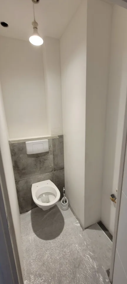 WC suspendu achevé, plaque de commande blanche sur un habillage en carrelage gris, sol encore sous film de protection