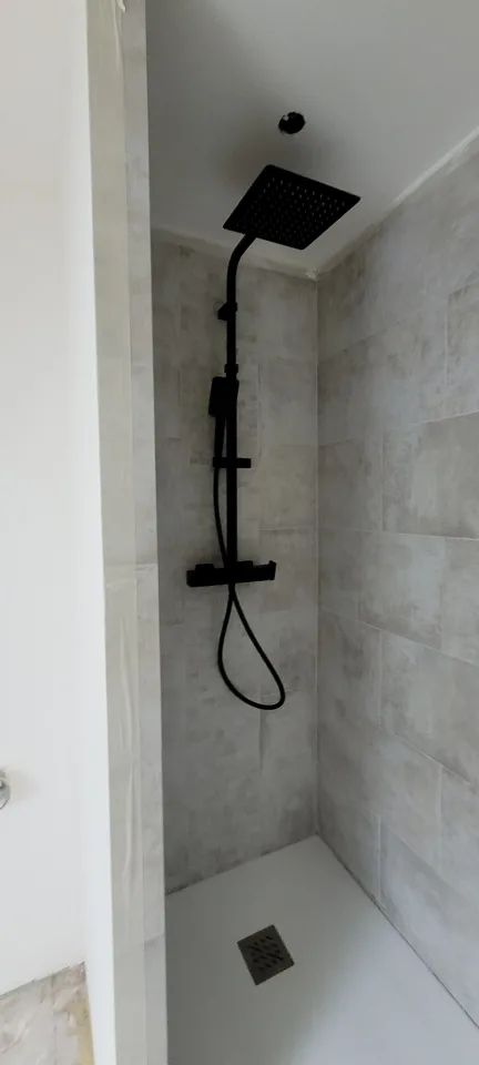 Gros plan sur la douche, colonne noire à pomme carrée, carrelage gris clair et receveur blanc