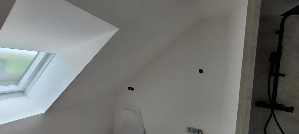 Salle d’eau sous les combles, fenêtre de toit dans le rampant et colonne de douche noire à droite