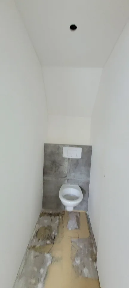 Autre WC sous rampant, cuvette suspendue devant un habillage en carrelage gris, sol pas encore fini