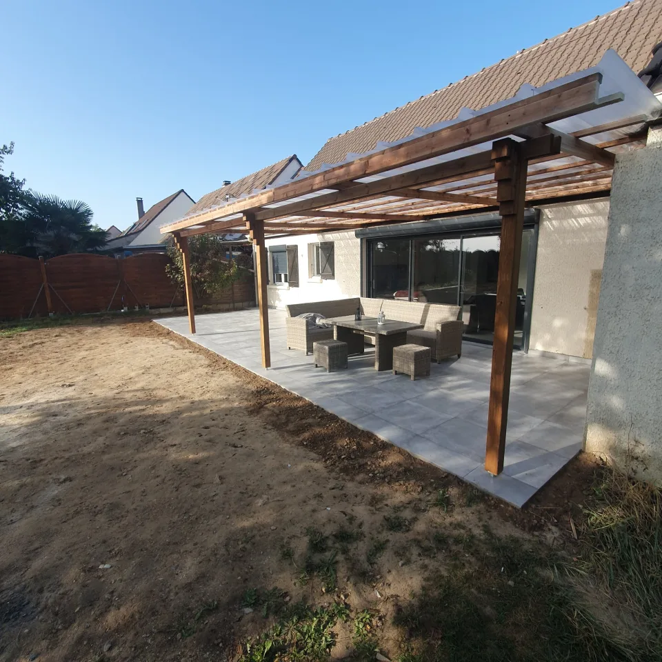 Terrasse livrée sous sa pergola en bois à couverture translucide, salon de jardin tressé devant la grande baie coulissante