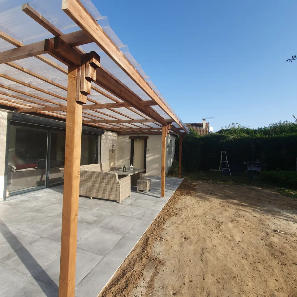 Vue sous la couverture translucide de la pergola, poteaux et chevrons en bois alignés jusqu’au fond de la terrasse