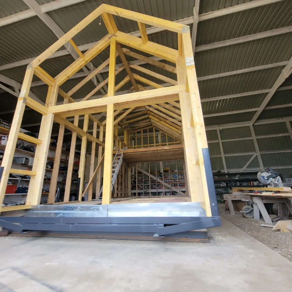 Pignon en ossature bois monté sur son châssis métallique dans l’atelier, chevrons posés, échelle vers le niveau de la mezzanine