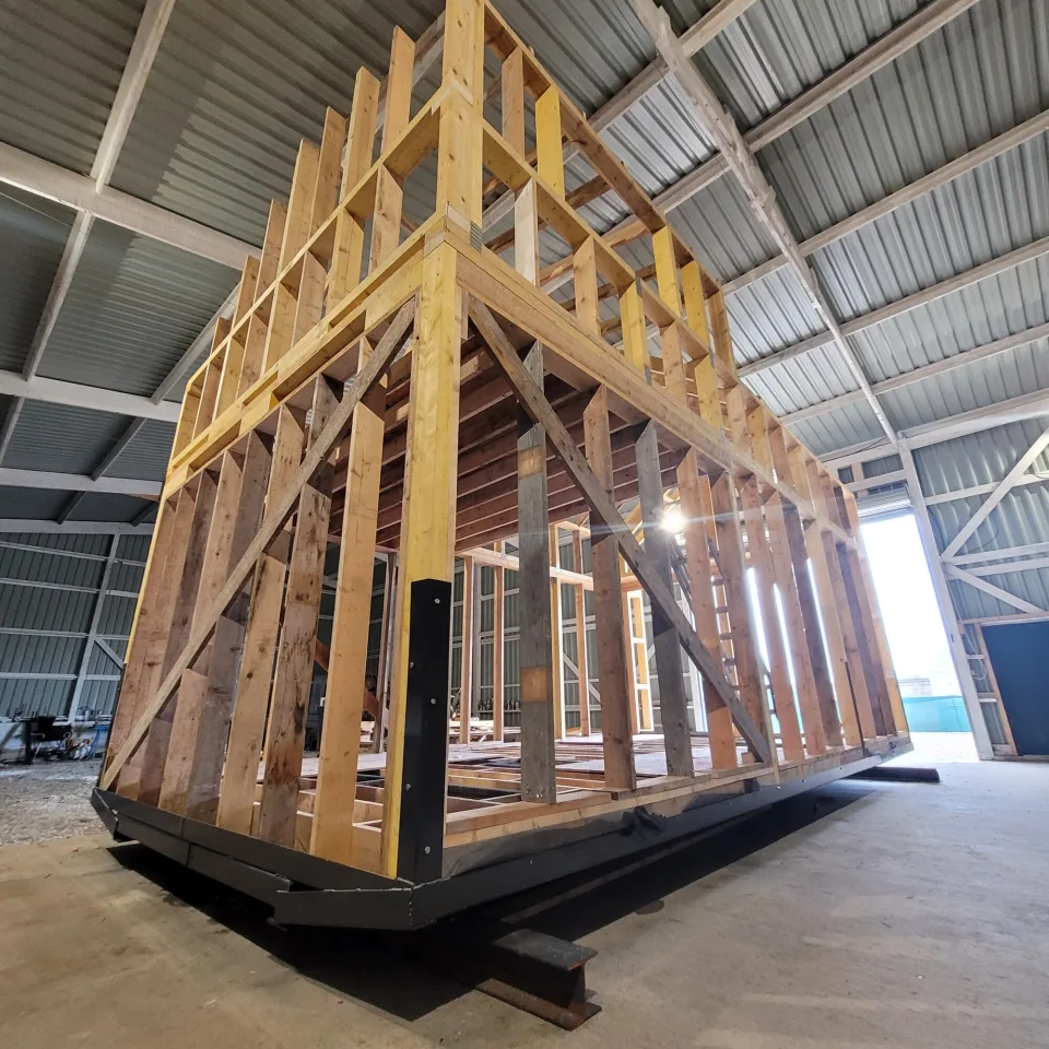 L’ossature vue en angle, montants, écharpes de contreventement et solives de la mezzanine, portail de l’atelier ouvert à droite