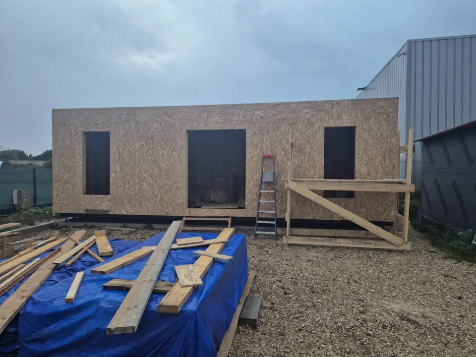 Murs fermés en panneaux OSB avec les ouvertures des fenêtres et de la porte-fenêtre, échafaudage et bois de chantier au premier plan