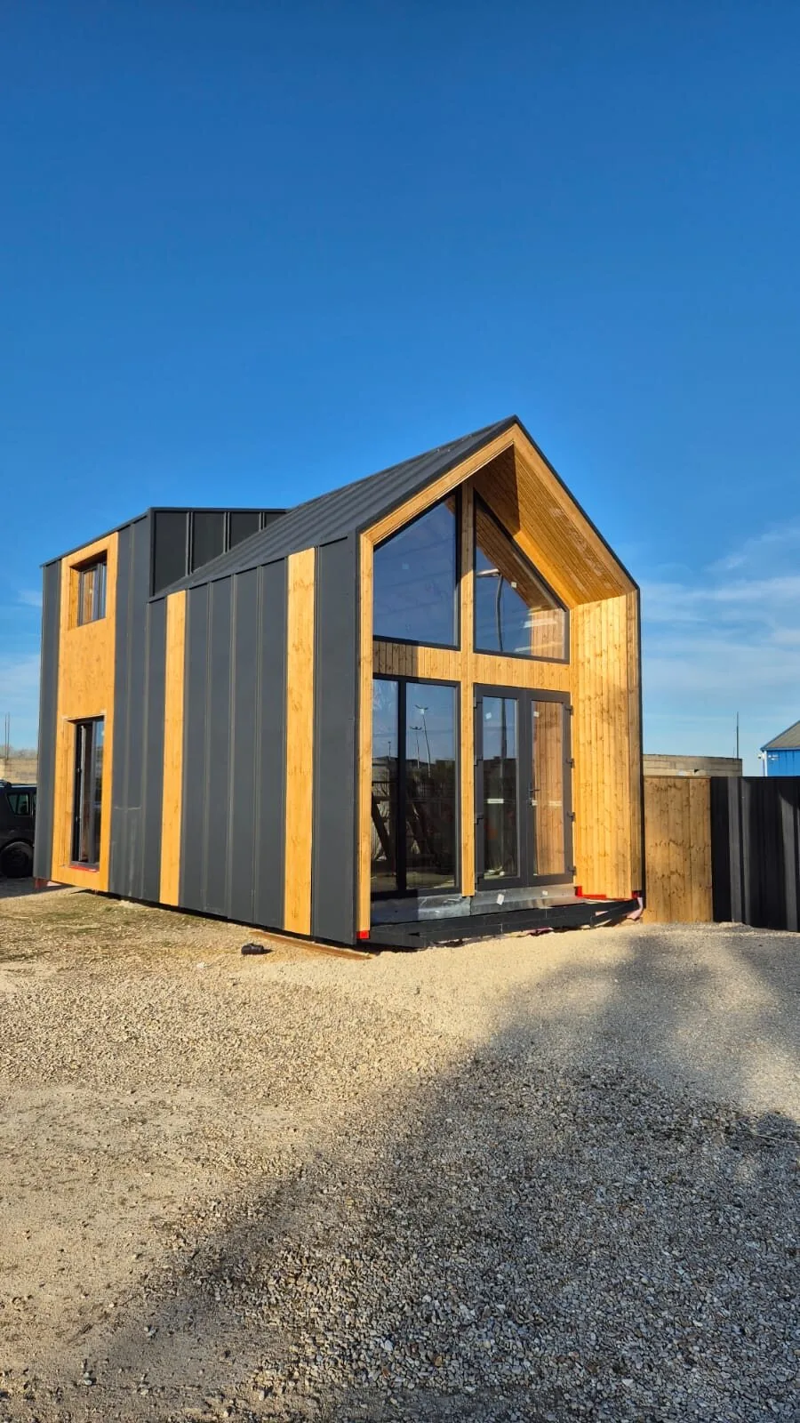 La maison achevée, pignon entièrement vitré encadré de bois, bardage métal anthracite et lames de bois naturel, toit noir à joints debout