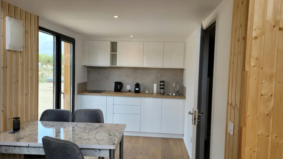 Cuisine blanche à plan de travail en bois, table au plateau effet marbre et porte vitrée donnant dehors