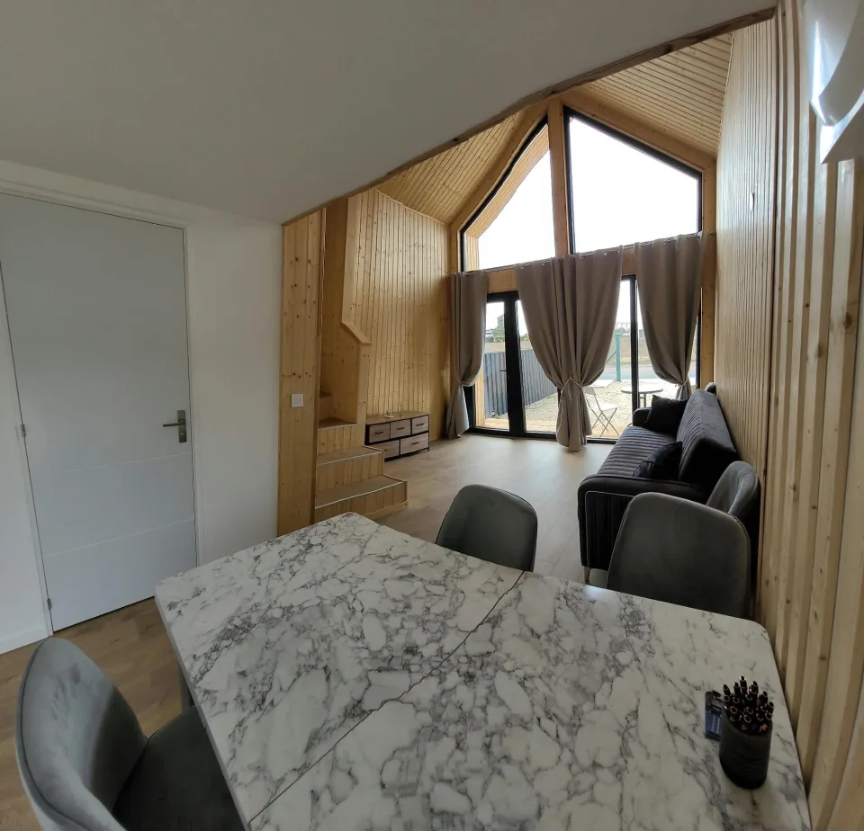 Le pignon vitré vu depuis la table, grandes baies et porte-fenêtre sous le plafond lambrissé qui suit la pente du toit
