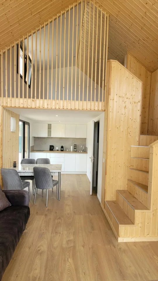 Le séjour en hauteur, mezzanine à lames verticales au-dessus de la cuisine et escalier en bois à droite
