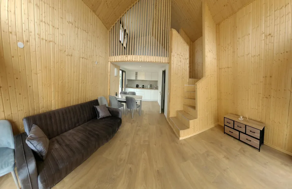 Séjour lambrissé, canapé, commode et escalier de la mezzanine, cuisine au fond