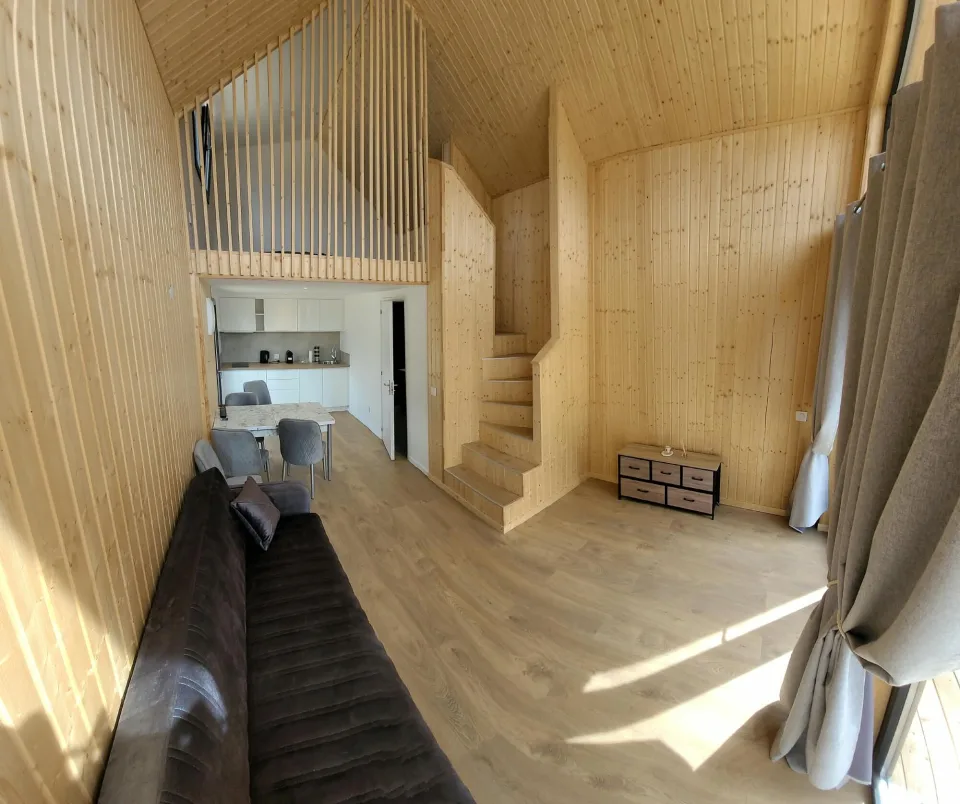 Le séjour depuis les baies, rideaux, canapé, escalier et mezzanine, cuisine au fond