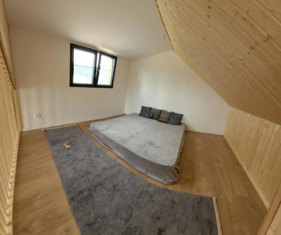 La chambre de la mezzanine, lit bas, tapis gris, fenêtre et rampant lambrissé