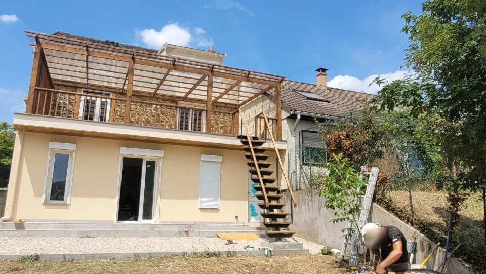 L’extension enduite et sa terrasse sous pergola en bois pendant les travaux, escalier extérieur en pose et jardin encore en terre