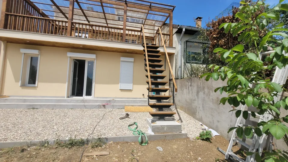 La façade de l’extension pendant les travaux, porte-fenêtre, volet roulant et escalier menant à la terrasse, échelle contre le mur voisin