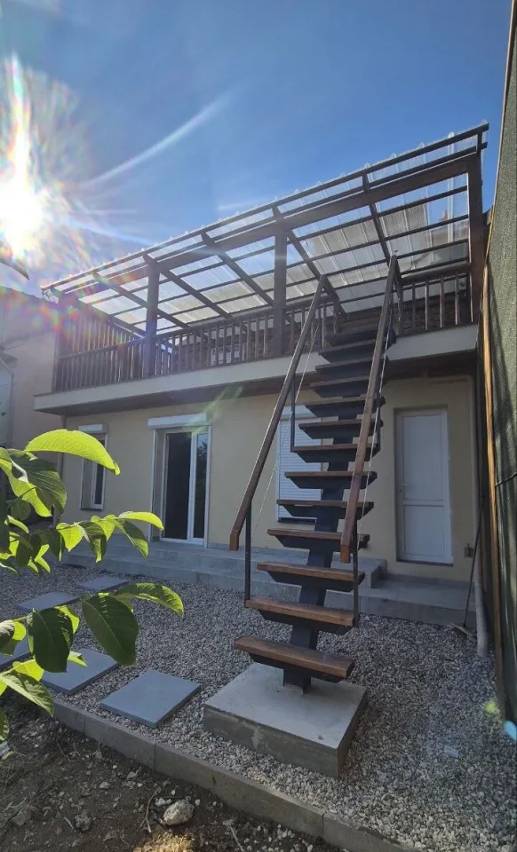 L’escalier extérieur et la terrasse en contre-jour, pas japonais dans le gravier au pied de l’extension