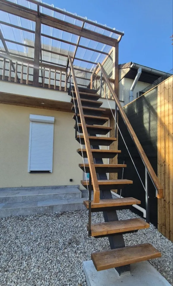 L’escalier extérieur de près, marches en bois sur limon central en acier, main courante en bois et câbles